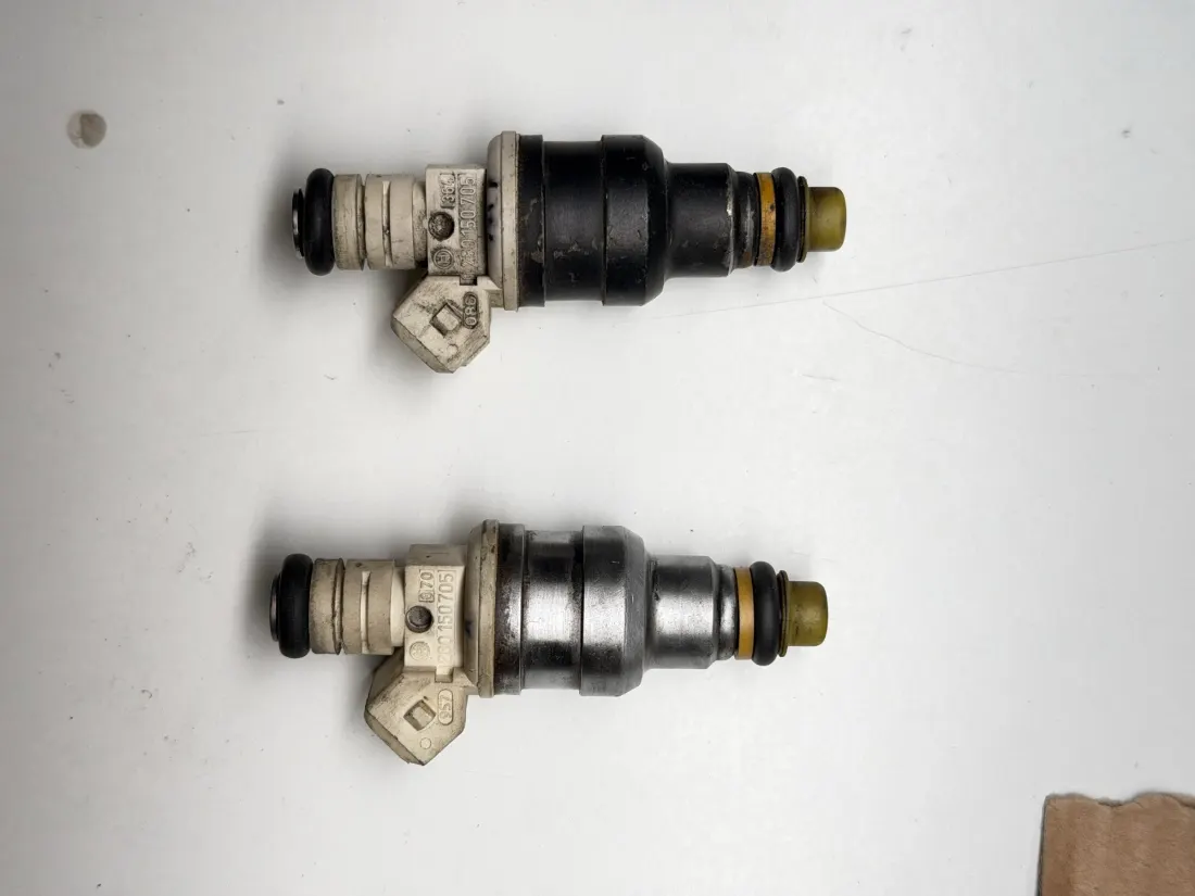 Two fuel injectors laid out on a white bench