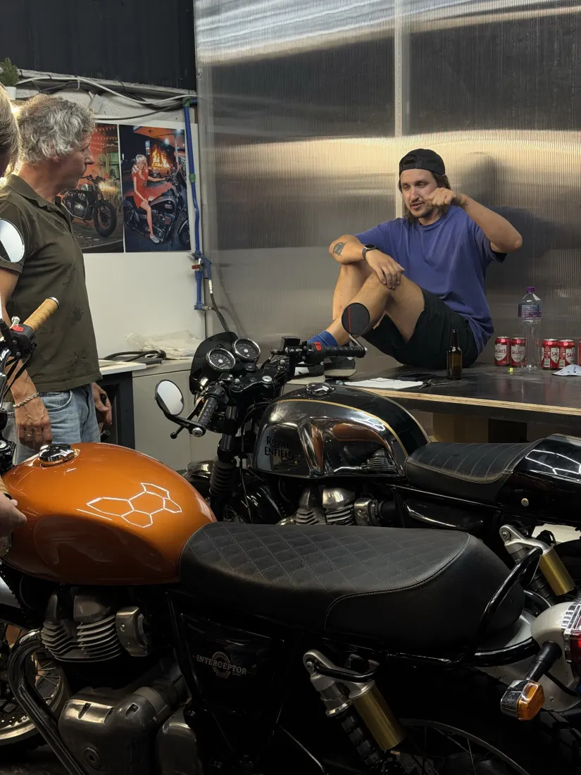 Riders chatting at the workbench next to an orange motorcycle