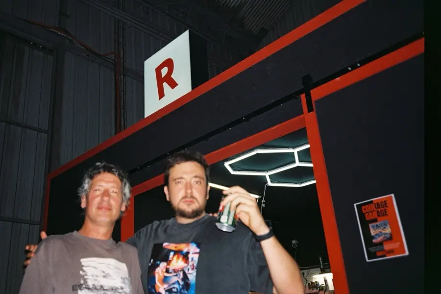 Two friends under the red R sign at the garage entrance, one raising a can