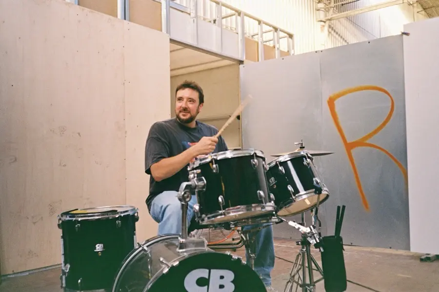 A drummer mid-beat at a kit with CB on the bass drum