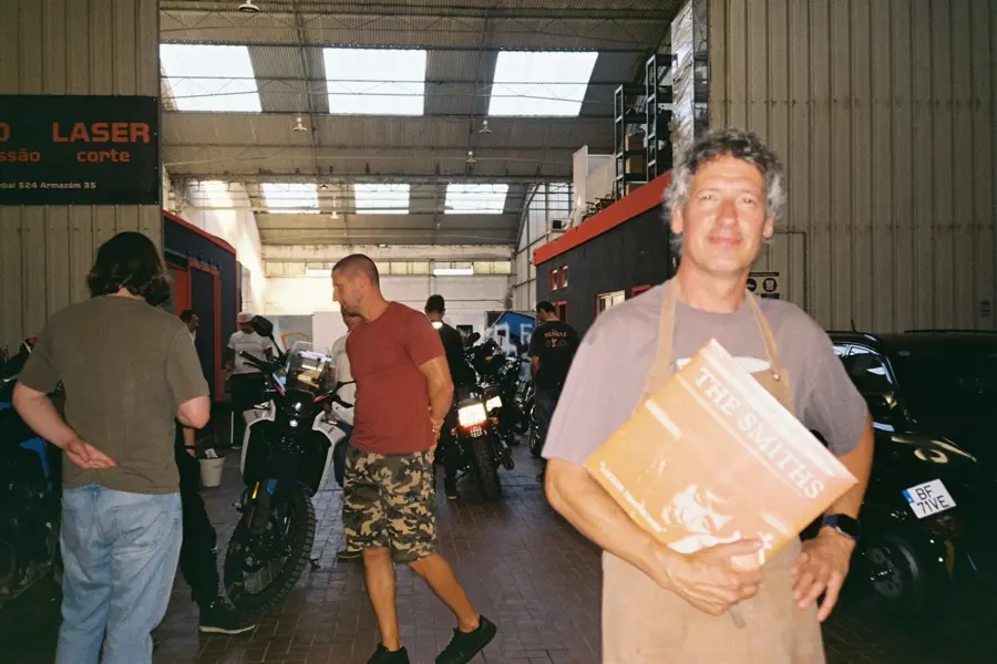 A friend in a canvas apron grinning at the camera, bikes and people behind