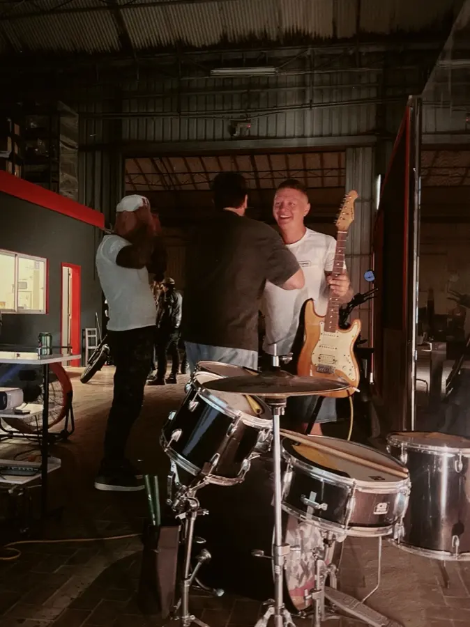 Friends around a drum kit and a guitar in the warm light of the garage